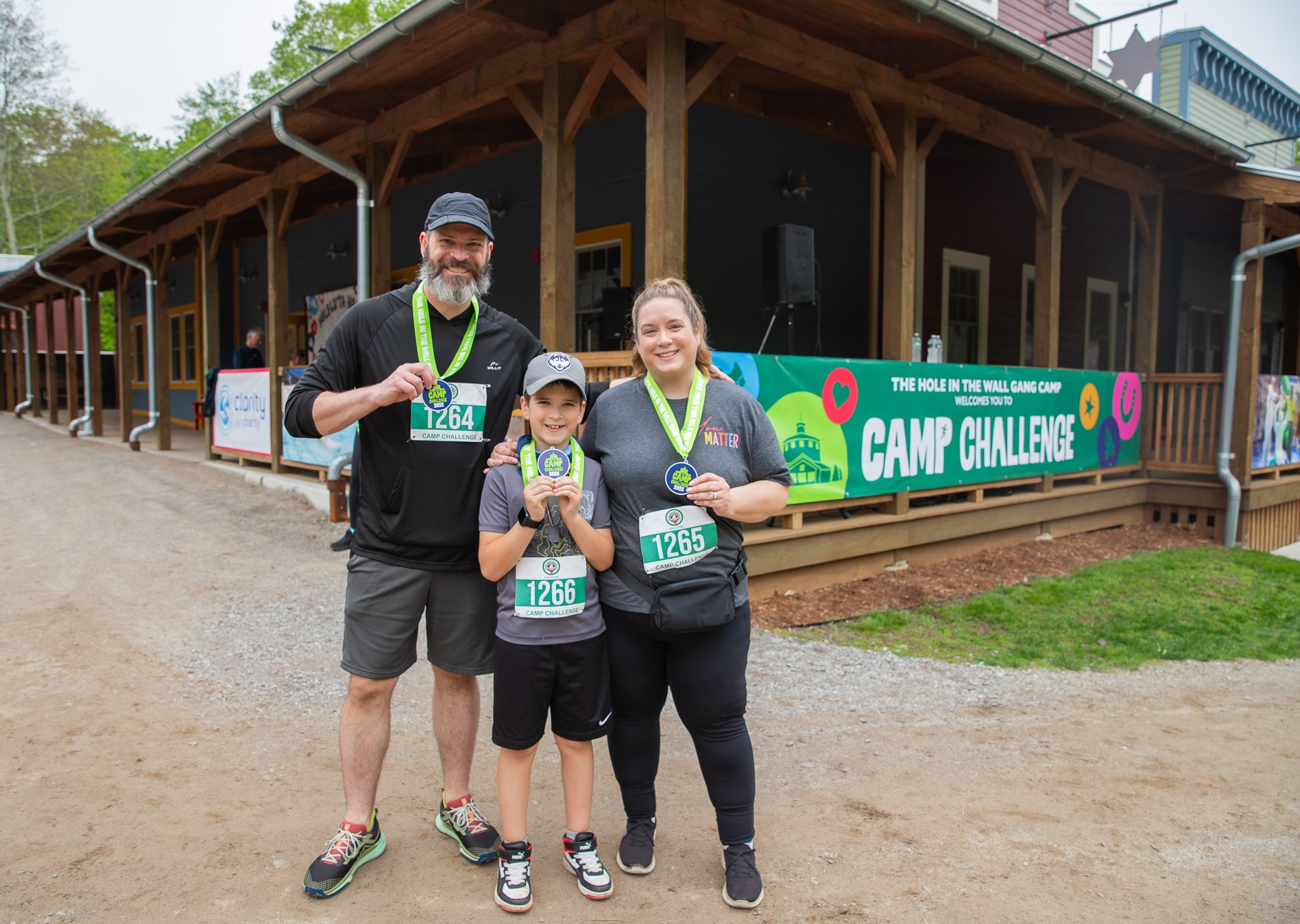 A family of three poses with their Challenge medals in front of the Creative Complex