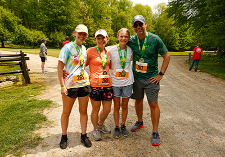 Family smiles at the camera wearing Camp Challenge medals on a sunny day at Camp