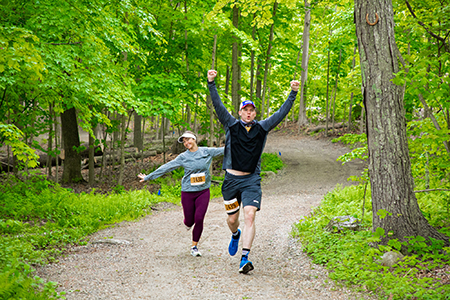 Two people run with arms raised through Camp's trails