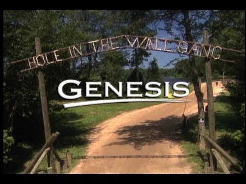 A dirt road passes under a rustic archway reading HOLE IN THE WALL GANG, with the word GENESIS overlaid in large white letters. Trees and blue sky are visible in the background.
