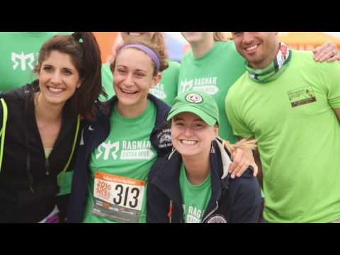 Four smiling people wearing green shirts and race gear pose closely together at an outdoor running event. One person is wearing a medal and race bib number 313. The background is slightly blurred.