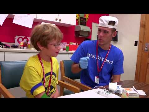 A young boy sits in a chair while an adult in a Fun Day 2012 shirt and gloves prepares medical supplies in a brightly colored room.
