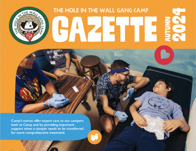 A nurse in blue gloves tends to a smiling boy lying on a medical table, while two adults, also smiling, reassure him. The scene is cheerful, inside a colorful camp setting, featured on a camp newsletter cover.