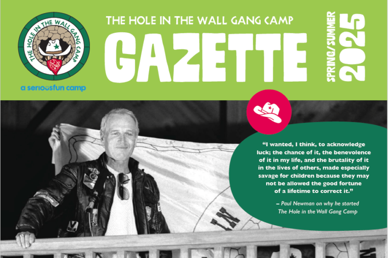 A black-and-white photo of a man on a porch holds a flag. Text reads: GAZETTE, Spring/Summer 2025 with a quote about acknowledging luck and helping children. Hole in the Wall Gang Camp logo appears at top left.