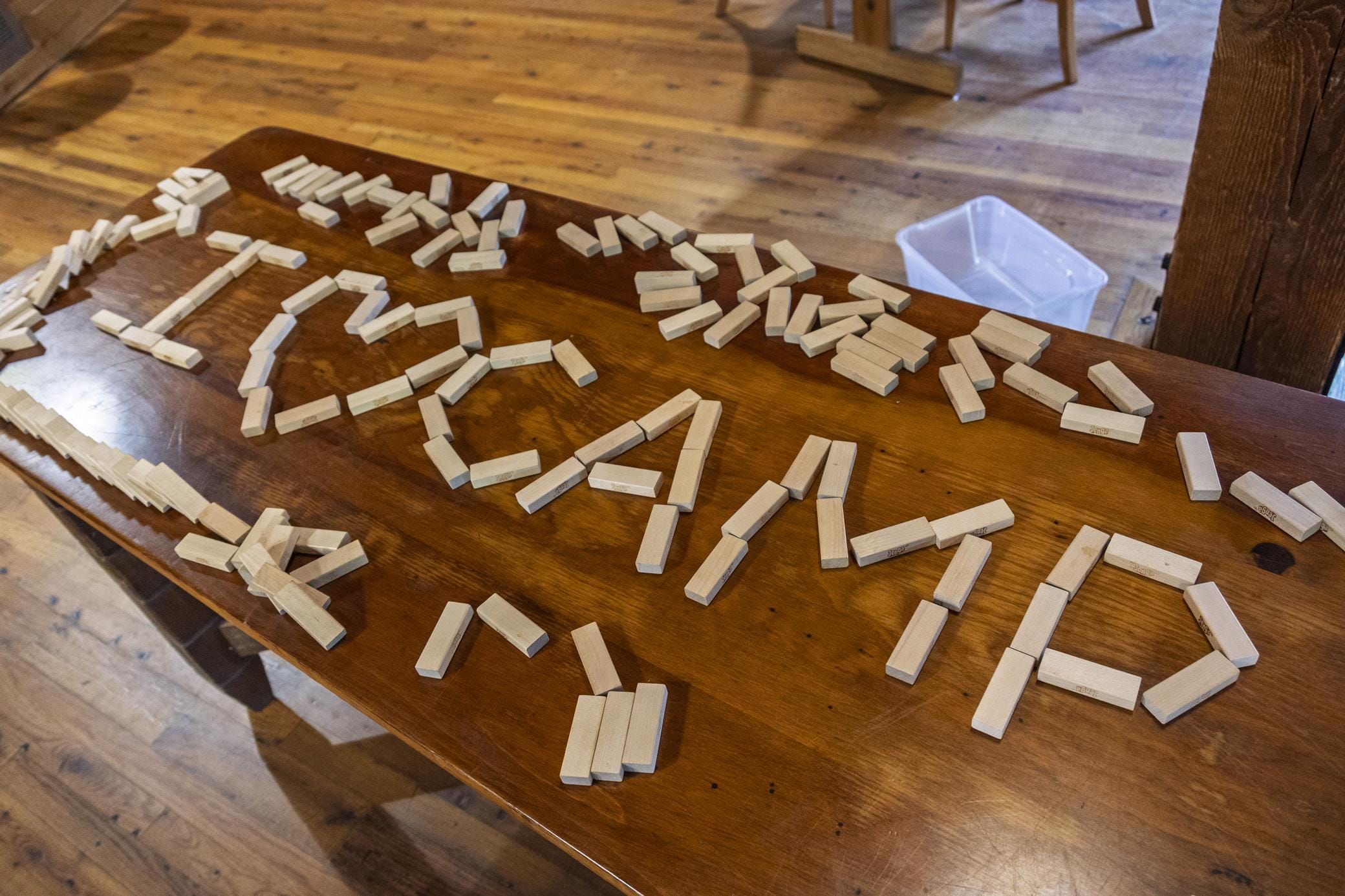 Dominoes arranged on a wooden table to spell out I ♥ AMD with some scattered pieces around; wooden floor and furniture are visible in the background.