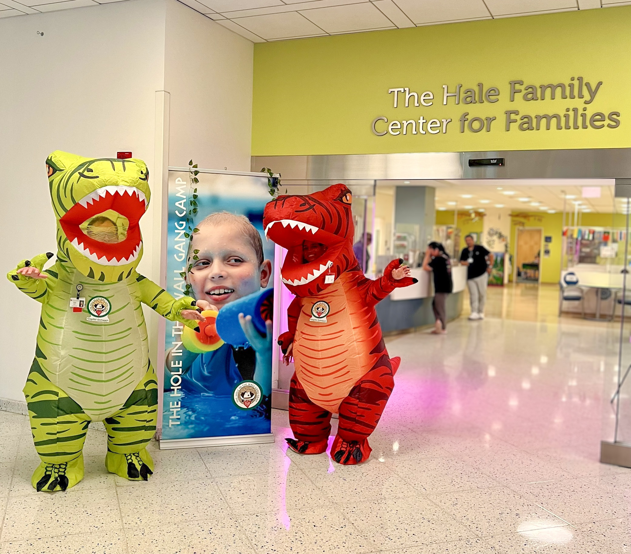 HOP specialists dressed in dinosaur costumes wave to the camera while at Boston Children's Hospital